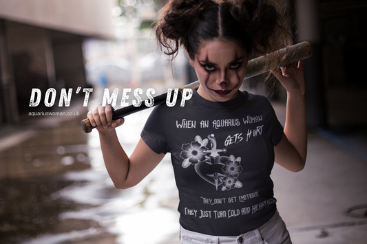 A fierce woman with intense clown makeup holds a bat over her shoulder, wearing a bold "When an Aquarius Woman Gets Hurt" t-shirt. The gritty urban setting and defiant stance embody strength, rebellion, and emotional resilience.